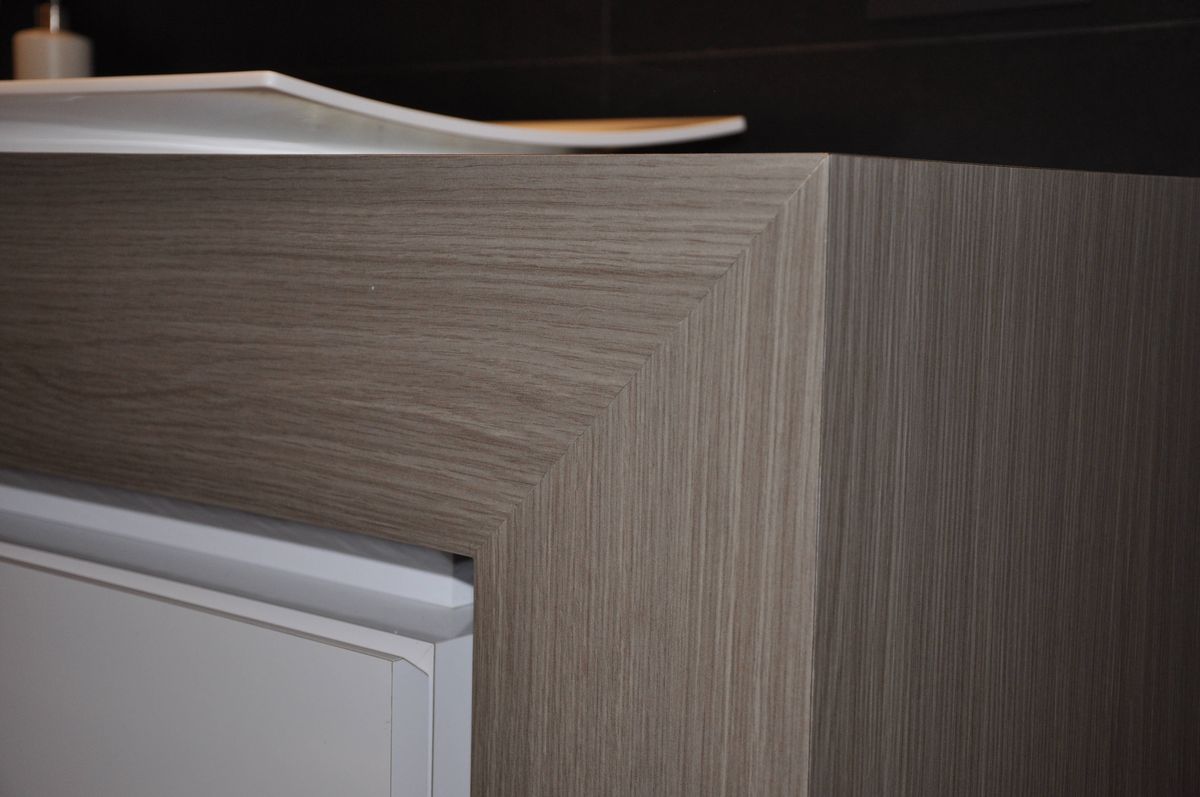 Detail van het houtkleurige tablet in verstek boven een witte lade met greeplijst