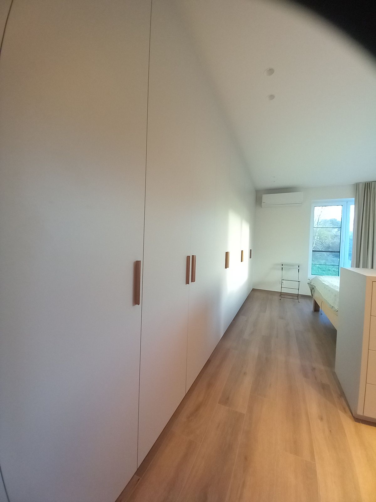 Lange grijze kastenwand in door en door grijs laminaat met verticale messing flapgrepen