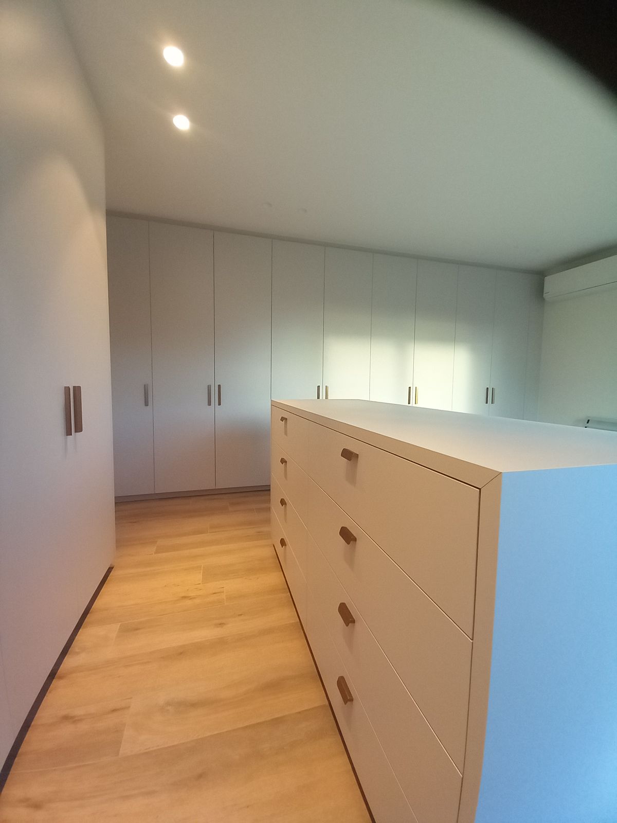 Grijze kastenwand achteraan en vrijstaand ladenmeubel met messing grepen op een houten vloer