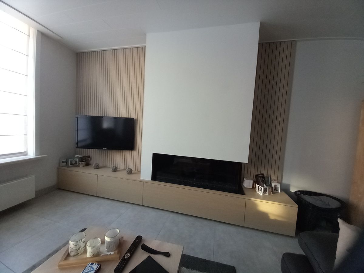 Moderne haardwand in Ieper met lange lage kast in shinnoki, witte schouw in mdf en verticale latten rond de televisie