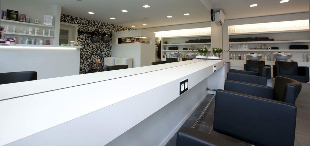 Kapsalon in Ieper met lange witte toonbank, zwarte kappersstoelen, wandrekken en zwart-wit behang