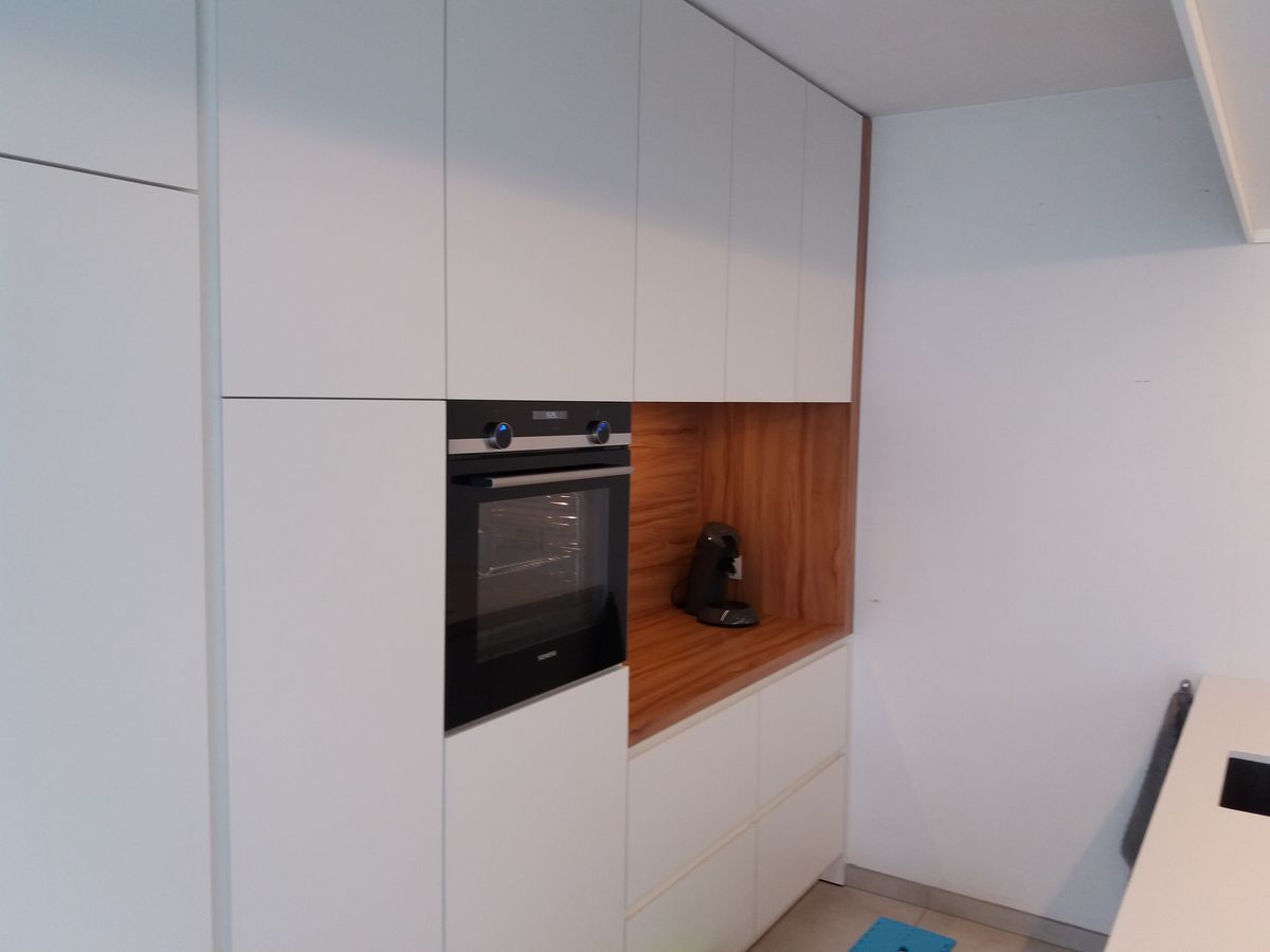 Witte hoge kasten in laminaat met ingebouwde oven en een houtkleurige nis met koffietoestel