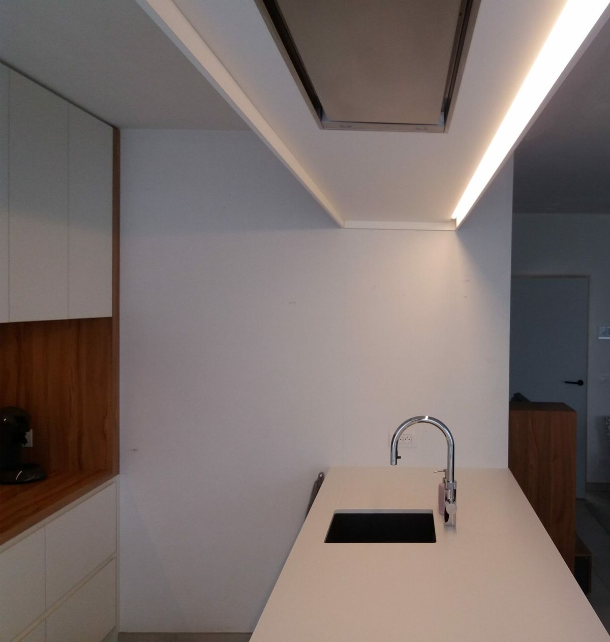 Wit eiland met spoelbak onder een verlaagd plafond met dampkap en indirecte ledverlichting