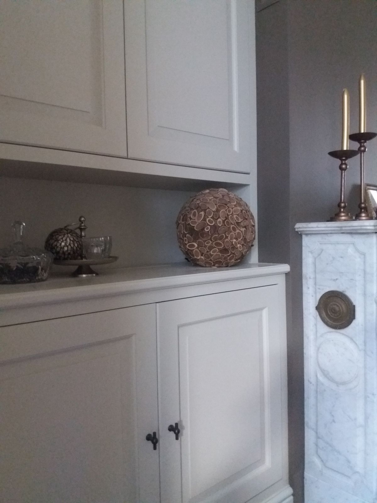 Detail van witte paneelkasten met zwarte knoppen en een nis naast de marmeren schouw