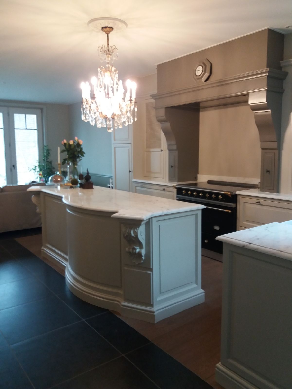 Klassiek Engelse keuken in Wevelgem met gebogen eiland, marmeren werkblad, grote schouw boven fornuis en Franse kroonluchter