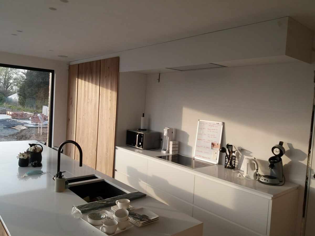 Witte keuken met eiland, zwarte spoelbak en kraan, en hoge kast in dik eikenfineer naast de dampkap