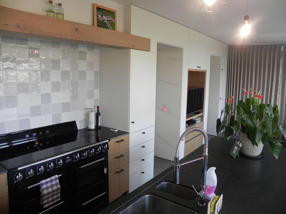 Keuken in Vlamertinge met zwart klassiek fornuis, witte en fineer kasten, geruite wandtegels en massief houten schap
