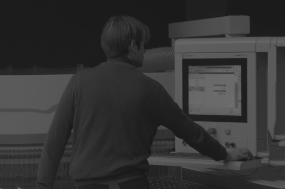 Zwart-witfoto van Lorenzo Bouwet op de rug gezien, terwijl hij een computergestuurde machine in het atelier bedient