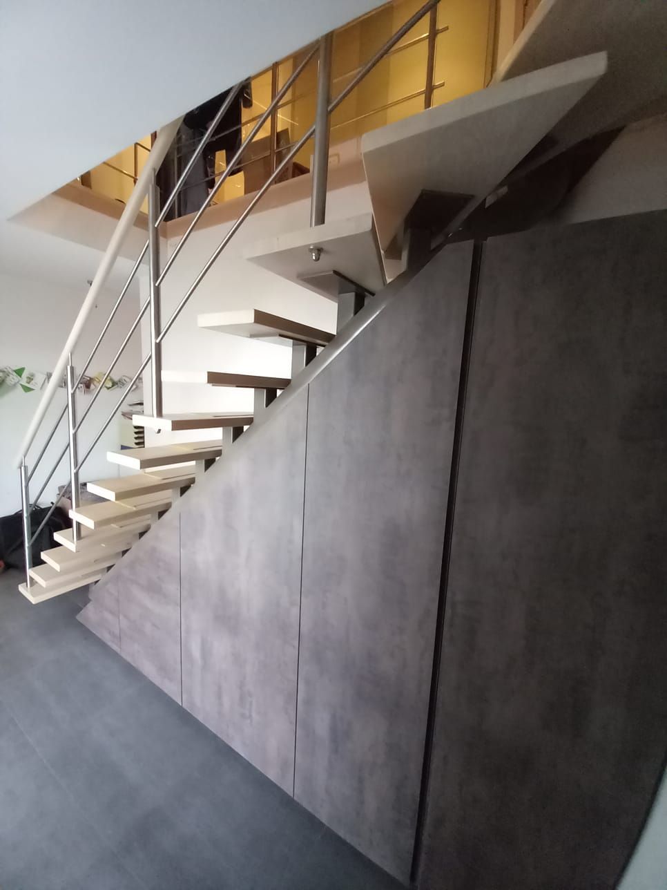Schuin aflopende kasten onder een open trap met houten treden, in donker betonlook laminaat