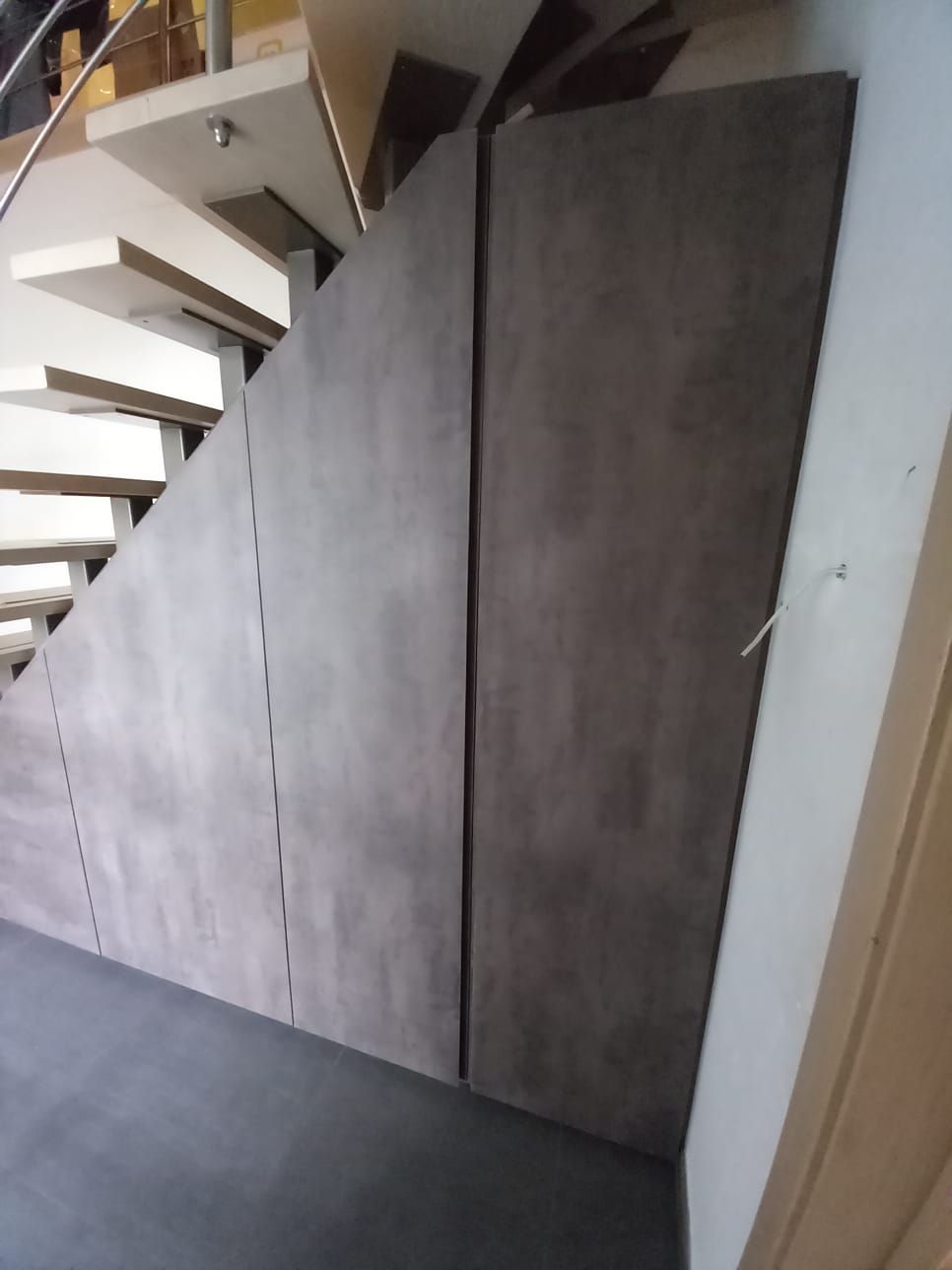 Kastenwand onder de trap met hoge deuren in donkergrijs laminaat, gezien vanaf de hal