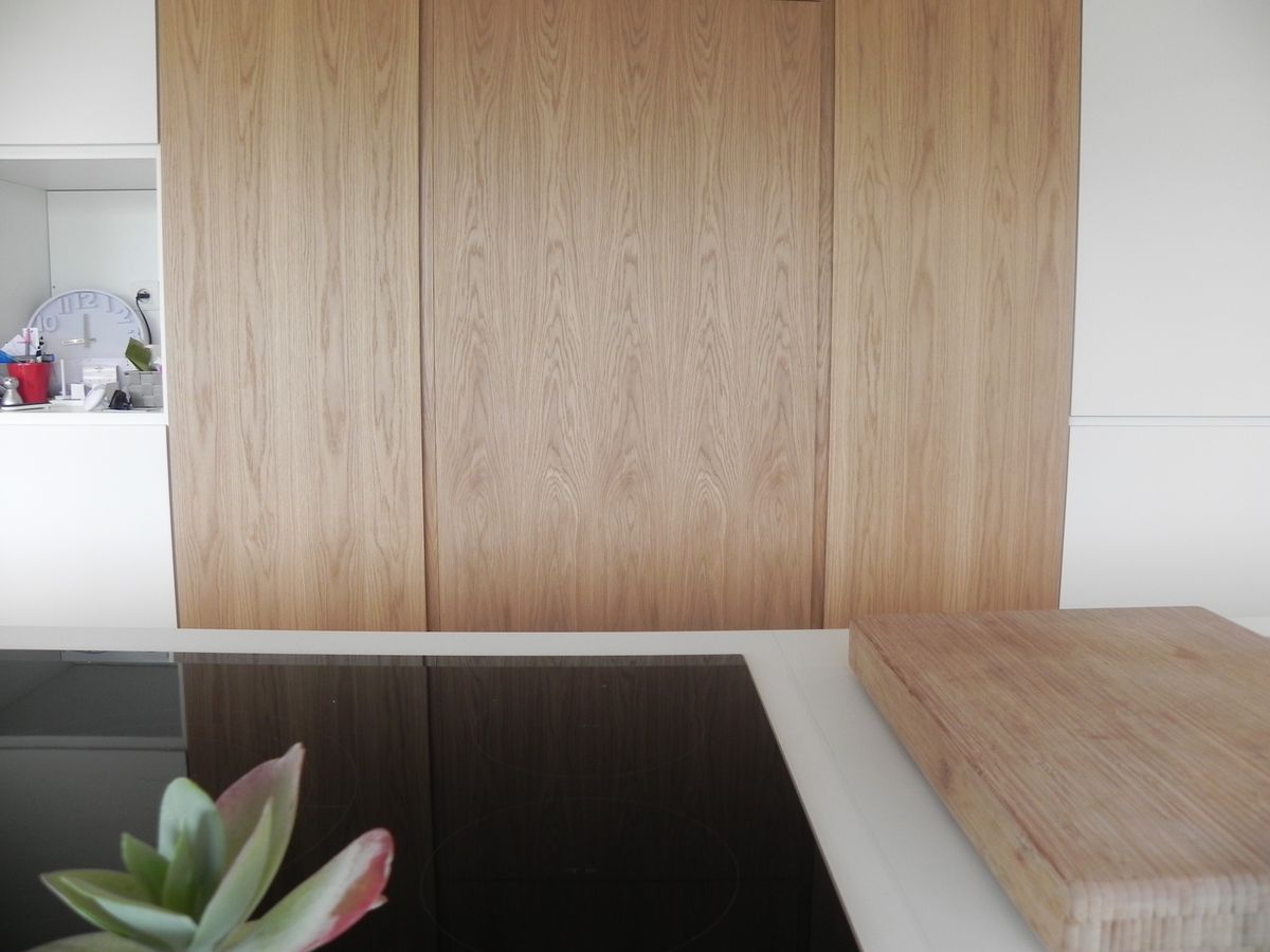 Kastwand in houtfineer met verticale deuren boven een wit werkblad met kookplaat