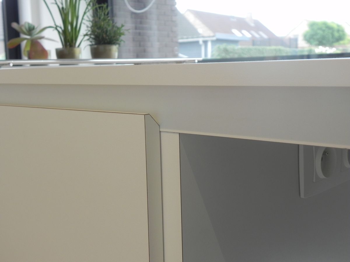 Detail van de afwerking van een wit werkblad en kastfront met stopcontact onder het raam