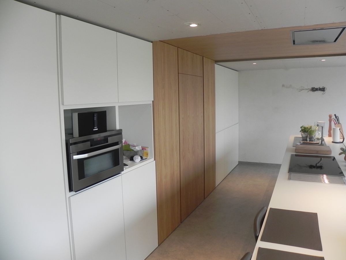 Witte hoge kasten met ovens en open nis naast een kastenwand en verlaagd plafond in contrasterend fineer