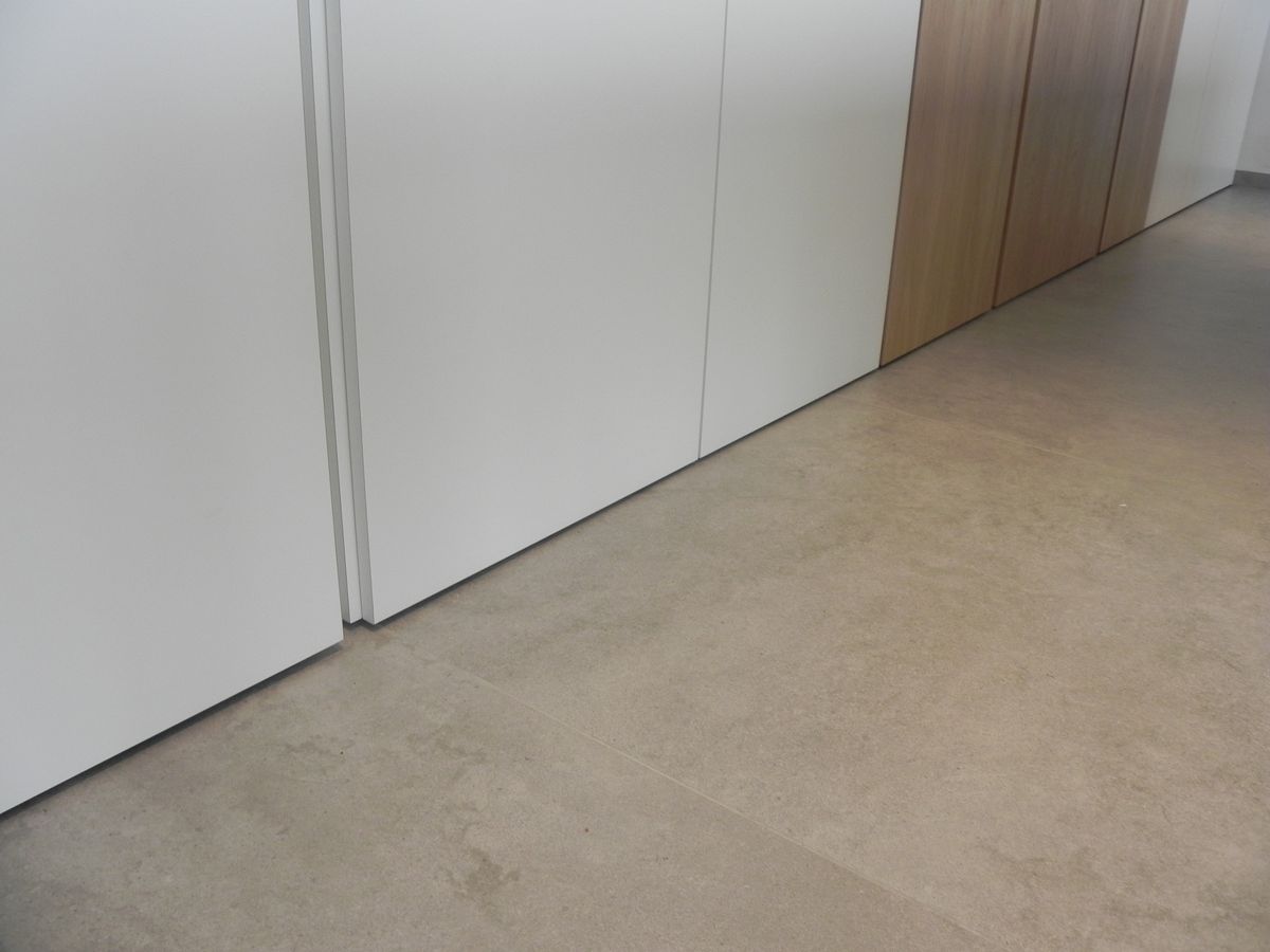 Grepenloze witte kastenwand op lichte vloer, overgaand in hoge deuren in fineer