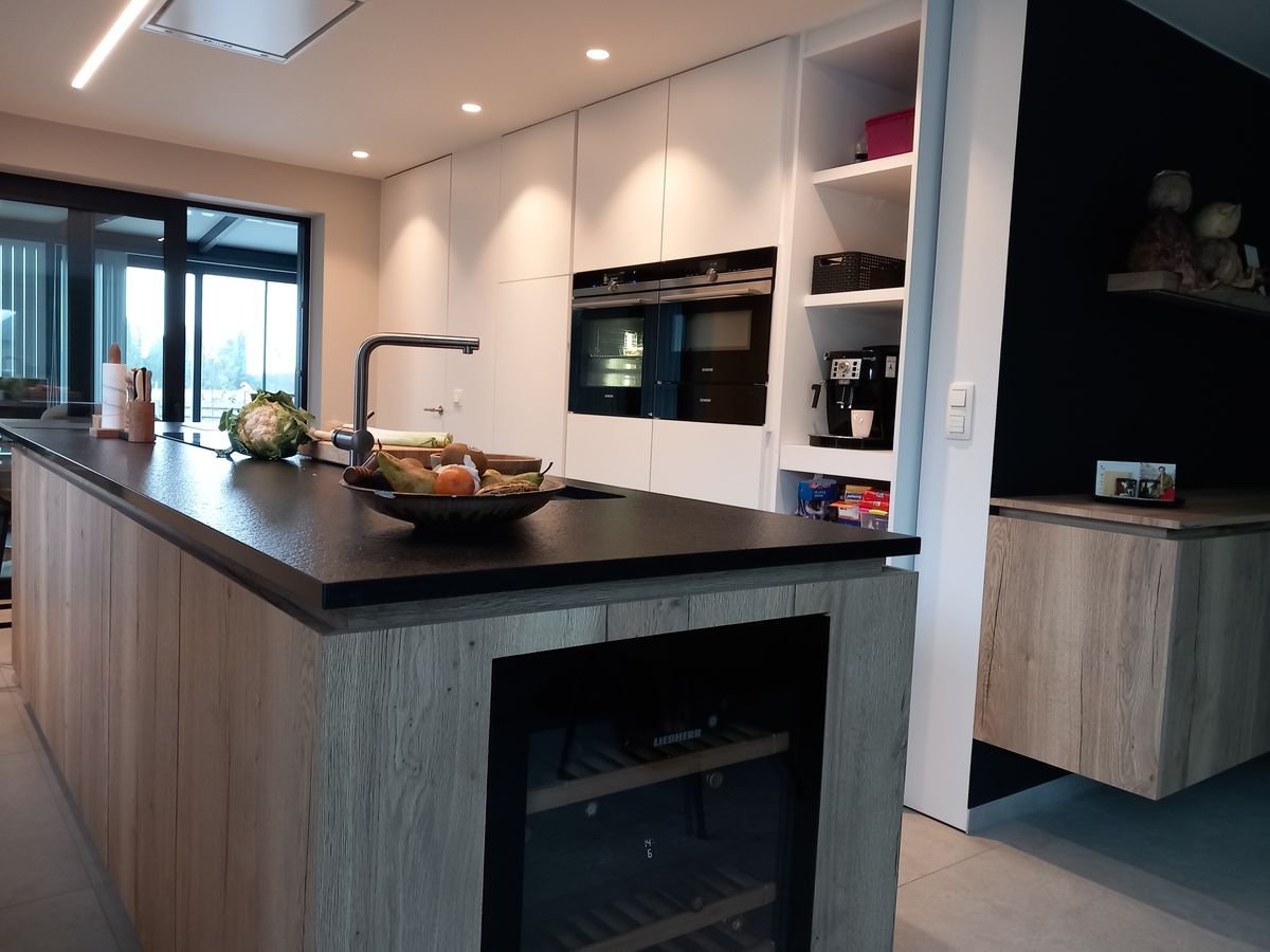 Kookeiland in gegroefd houtlook laminaat met ingebouwde wijnkoelkast, zwart werkblad en witte kastenwand met ovens