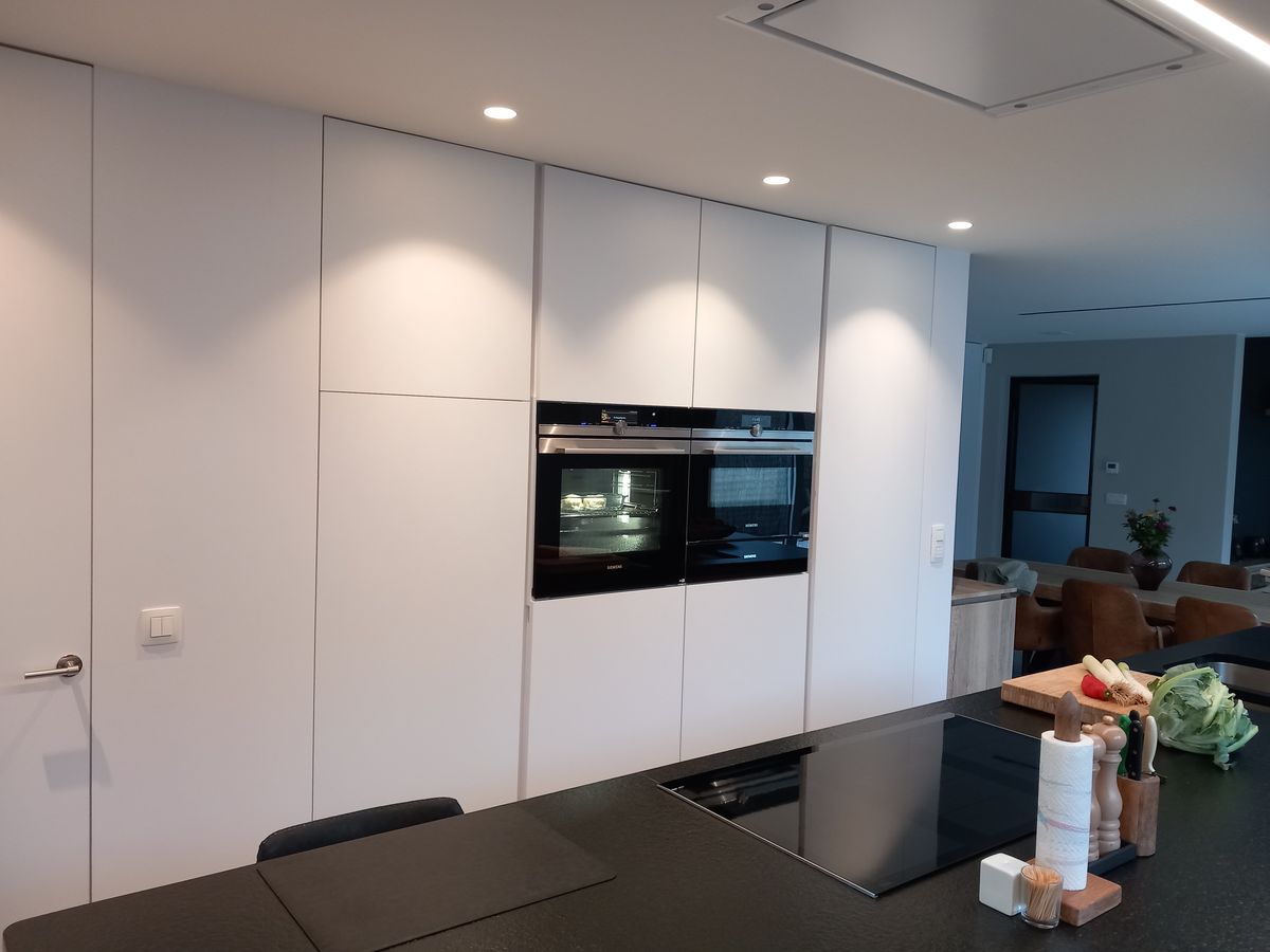 Hoge witte keukenkasten met twee ingebouwde ovens, inbouwspots en zwart werkblad met inductiekookplaat