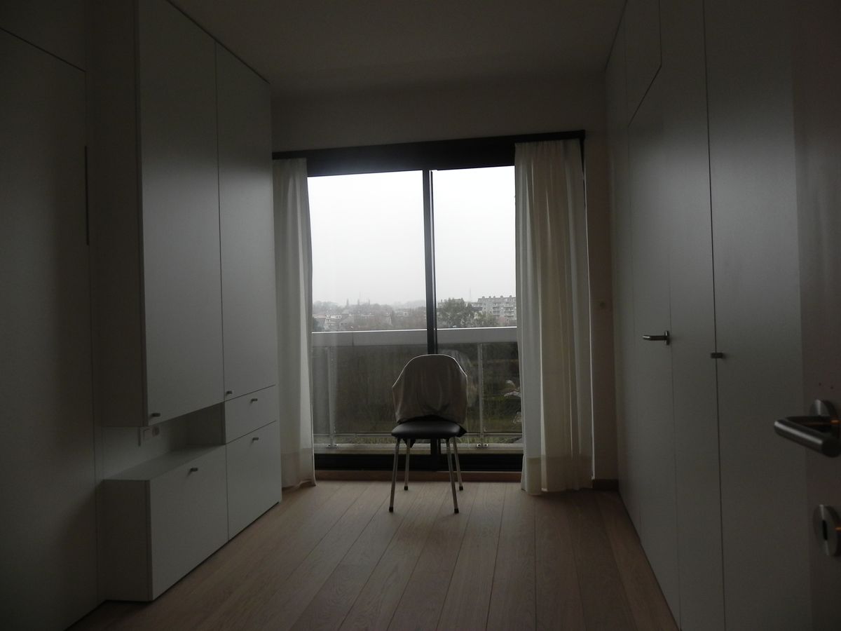 Slaapkamer met witte kastenwanden aan beide zijden en een groot raam met gordijnen