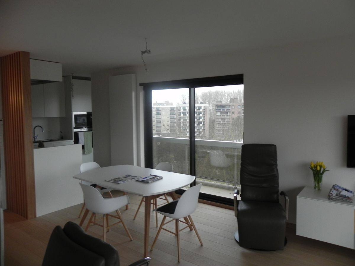 Open leefruimte met witte keuken, houten lattenafscheiding, eettafel met witte stoelen en groot raam met uitzicht