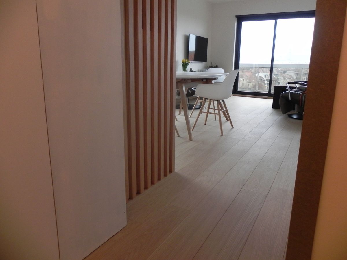 Doorkijk door de houten lattenafscheiding naar de leefruimte met eettafel en lichte houten vloer