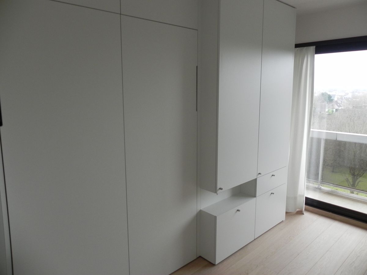 Witte inbouwkasten in de slaapkamer met open nis, lades en raam met uitzicht