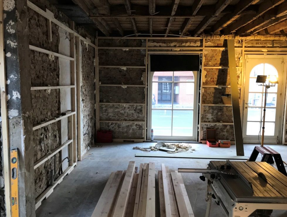 Situatie voor de renovatie: houten regelwerk tegen bakstenen muren en een zaagtafel in de lege ruimte
