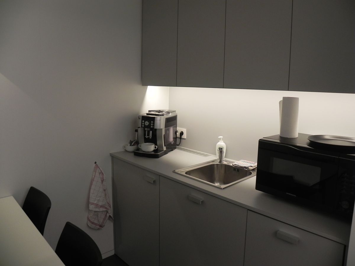 Minikeuken in zwart-wit laminaat met grijze bovenkasten, spoelbak, koffiemachine en ledverlichting onder de kasten