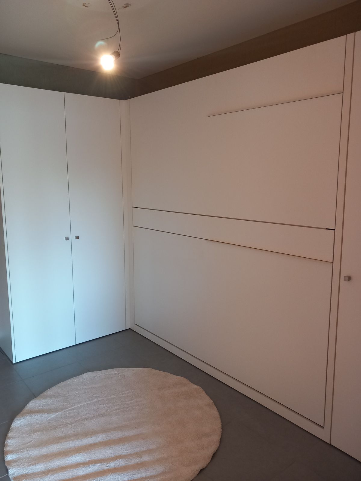 Witte kastenwand met dichtgeklapt stapelbed naast een hoge kast en een rond tapijt