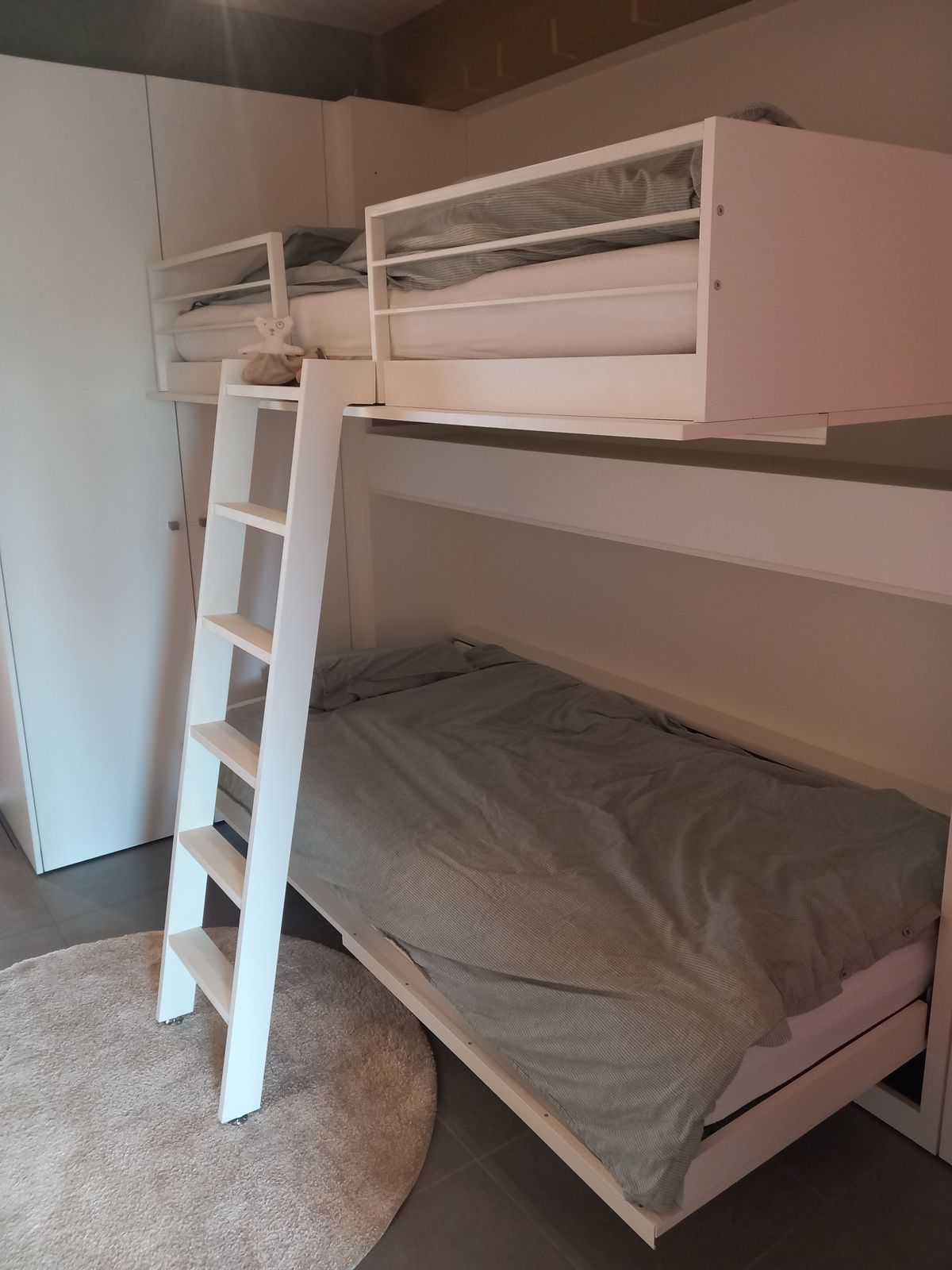 Opengeklapt stapelbed met witte ladder, bovenbed met reling en onderbed met grijs dekbed