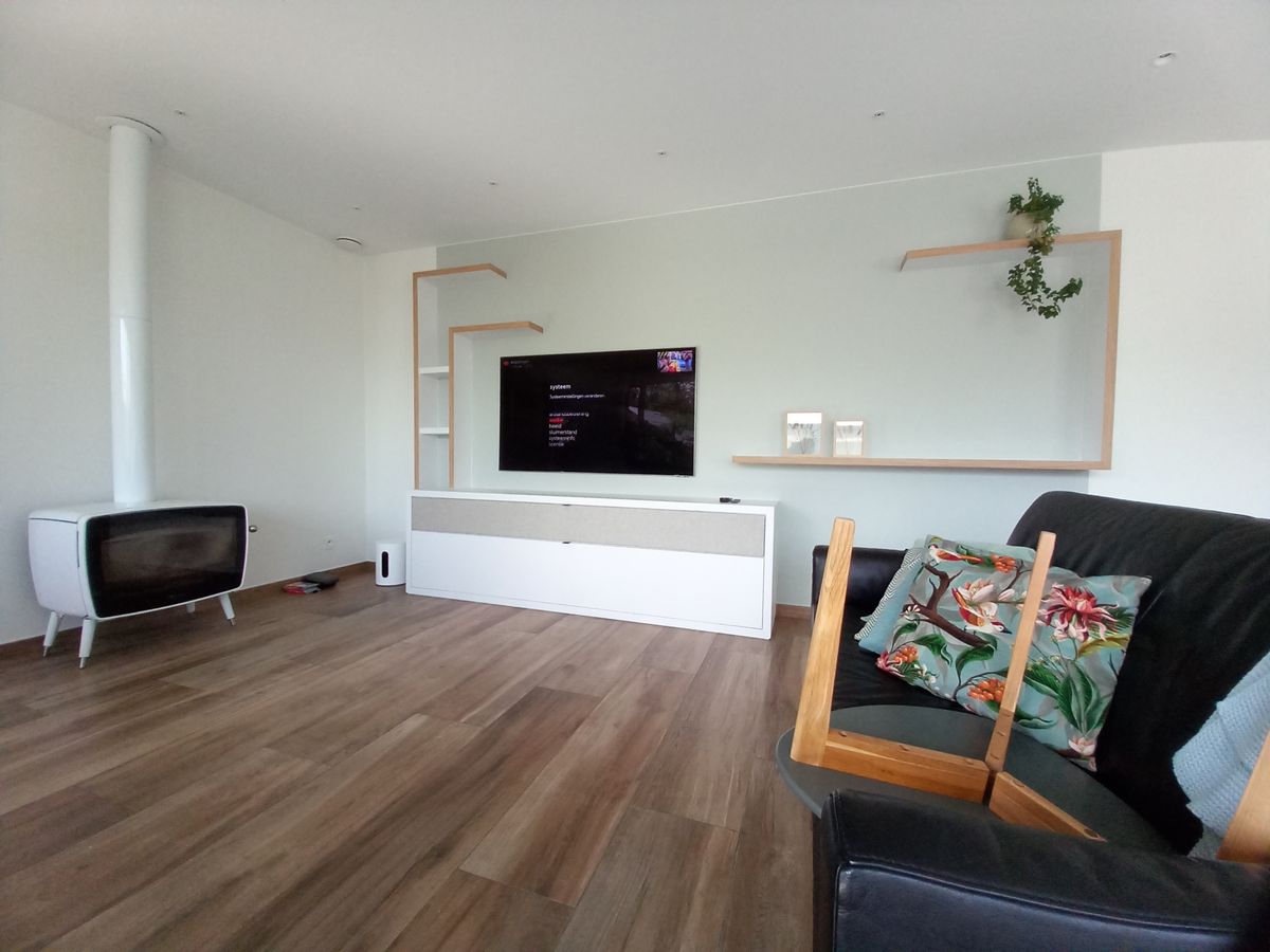 Woonkamer in Vlamertinge met wit laminaat tv-meubel, lichtgrijs akoestisch doek en houten wandplanken