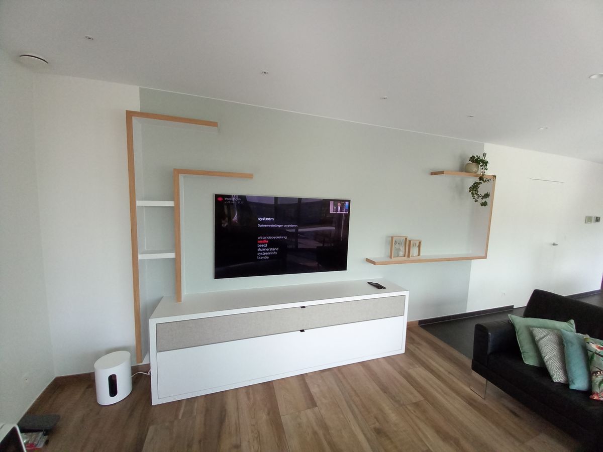 Laag wit tv-meubel met lade bekleed met geluiddoorlatend doek, houten kaders en planken aan de muur