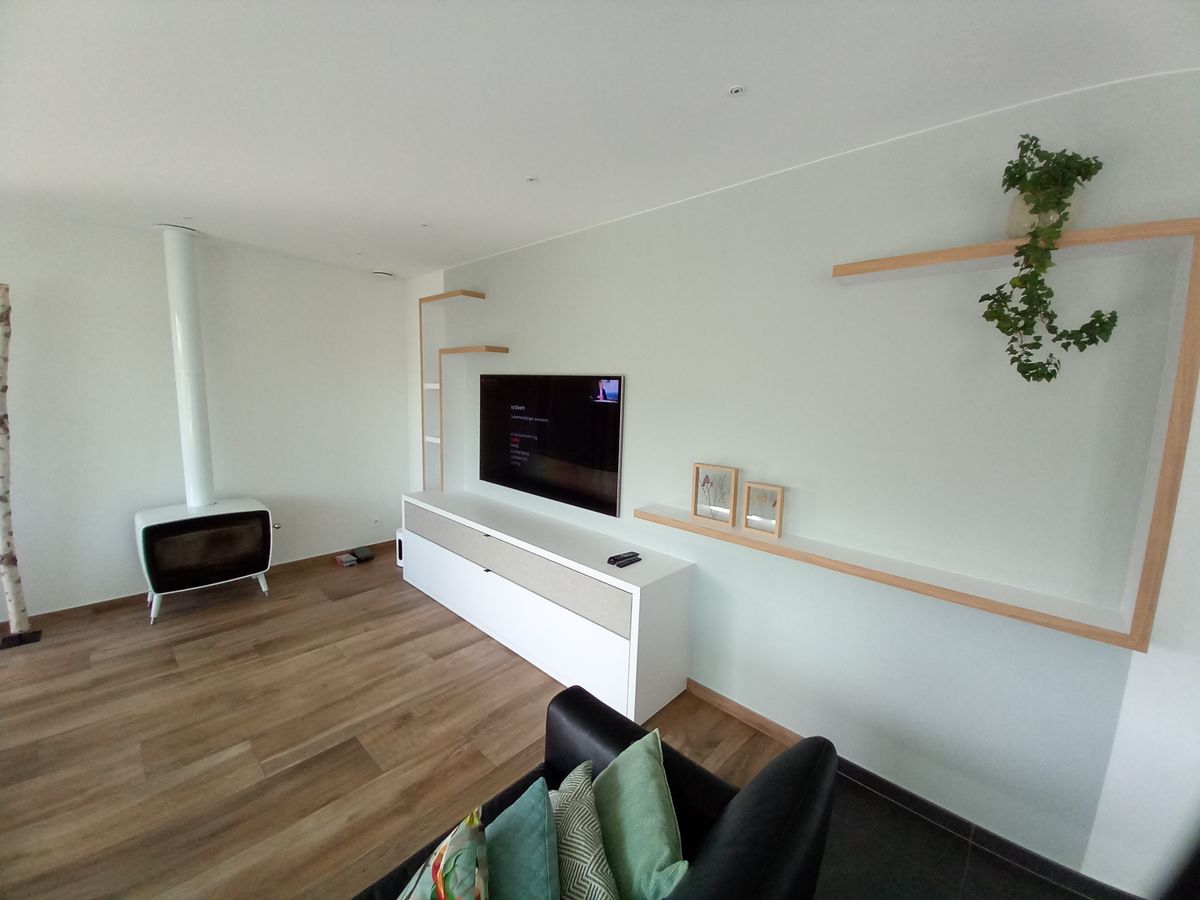Woonkamermeubel in door en door wit laminaat met houten wandplanken naast een witte kachel