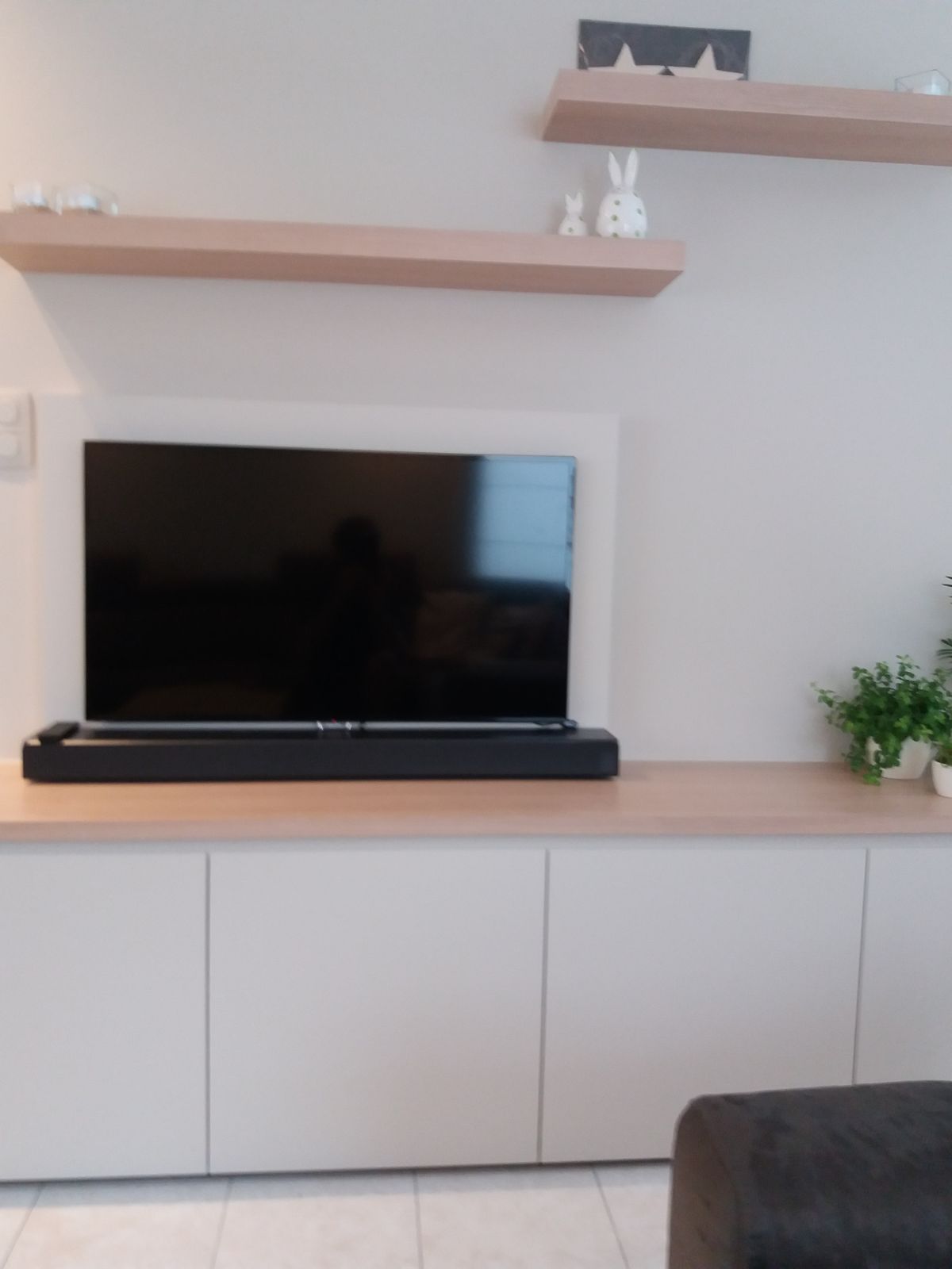 Vooraanzicht van het tv-meubel met witte kastdeuren, houtlook blad, tv-kader en wandplanken