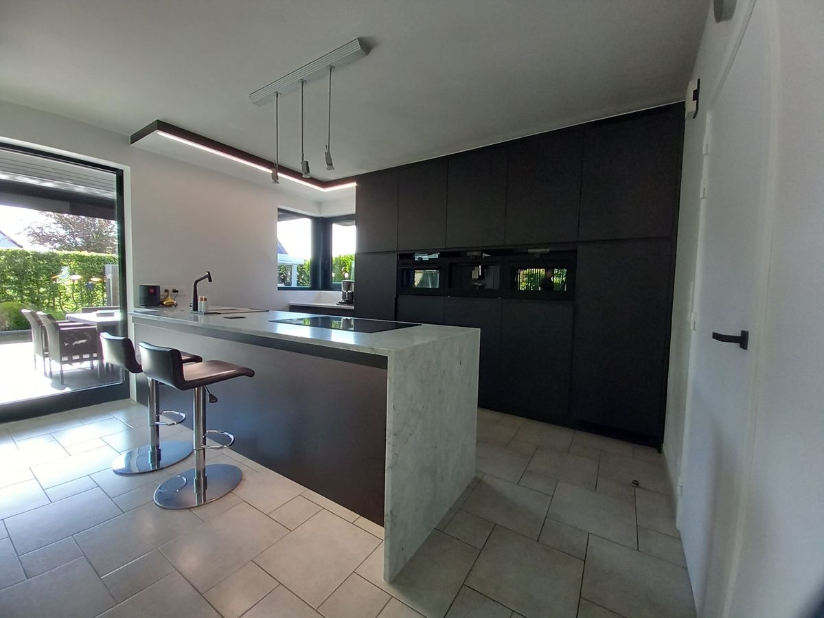 Zwarte keuken in Ieper in laminaat met eiland in Carrara-marmer met watervalzijde en hoge kastenwand met ovens